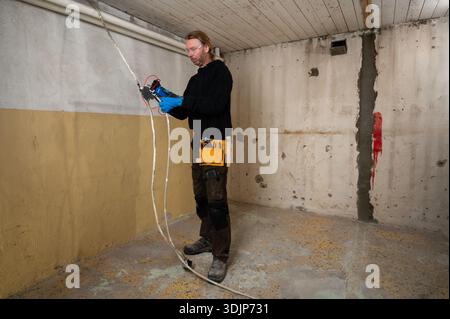 Electrician checking voltage on electrical cables during interior renovation, using testing equipment and wearing protective gloves Stock Photo