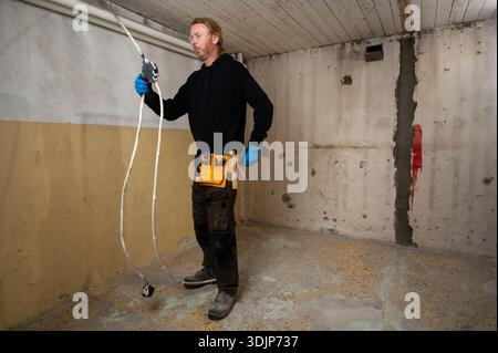 Electrician grabbing tool from tool belt while working on electrical junction box during interior renovation, wearing protective gloves Stock Photo