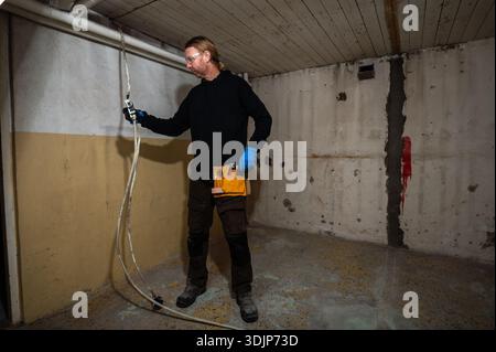 Electrician holding electrical cable while reaching for tool during interior electrical installation and renovation work, wearing protective gloves Stock Photo