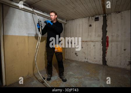Electrician working on electrical junction box with screwdriver during interior renovation, using professional tools and wearing protective gloves Stock Photo