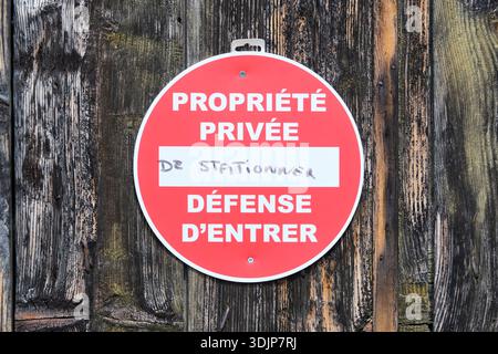 Red round sign on a weathered wooden door with French text Propriété privée Defense d'entrer and handwritten de stationner Stock Photo