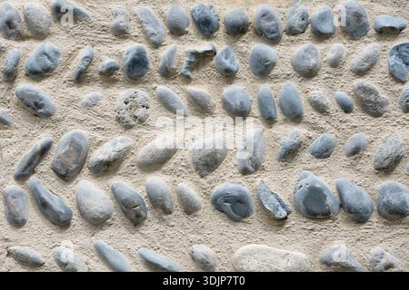 Background of a natural round river stone masonry wall with cement in Southern France. Detailed stone texture image in beige, brown, blue and grey Stock Photo