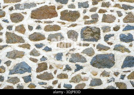 Background of a natural stone or sandstone masonry wall with cement in South France. Detailed stone texture image in beige, brown, grey and blue Stock Photo