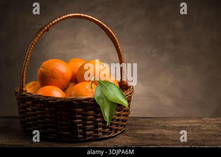 Bunch of ripe fresh orange fruits in a wicker basket on wooden table. Stock Photo