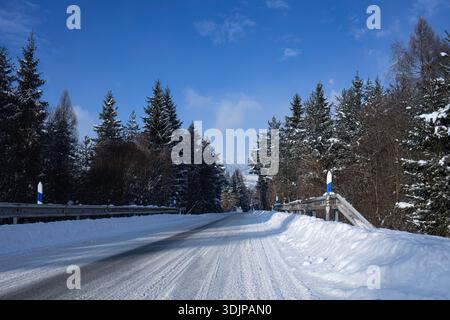 Snowy Winter Road Through Forest Under Blue Sky Stock Photo