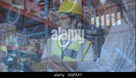 Reviewing tablet, warehouse worker in yellow hardhat neon vest checking stock with AR HUD Stock Photo