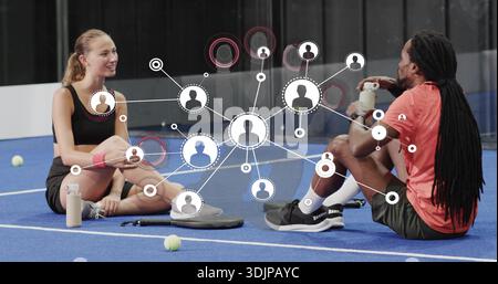 Sitting couple in athletic clothes resting on blue court, with tennis balls and network overlay Stock Photo