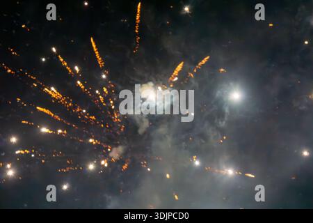 Abstract view of a fireworks explosion with glowing sparks and smoke against a dark night sky. Stock Photo