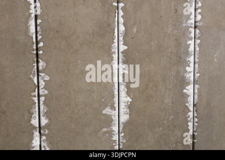 Detailed texture of gray precast concrete wall panels with vertical seams filled with rough white plaster lines showcasing unfinished construction sur Stock Photo