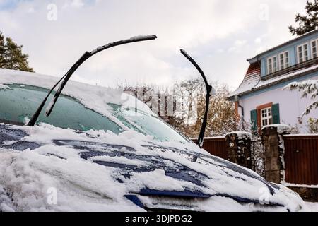 Snow covered car windshield with raised wiper blades, parked in residential street Stock Photo