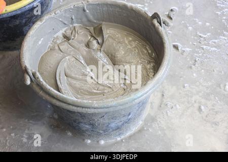 Close up view of wet grey cement mixed in plastic bucket for construction work showing unfinished raw material texture and industrial gritty feeling o Stock Photo