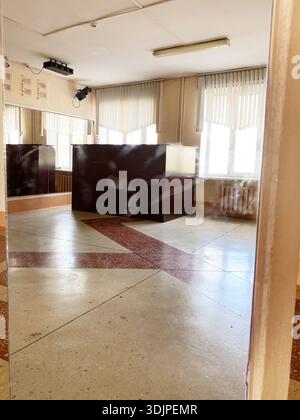 A child's handprint is seen on a mirror in an old school hall featuring wooden furniture, large windows, and patterned flooring that adds character Stock Photo