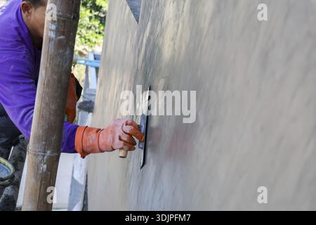 Construction worker carefully plastering grey concrete wall using trowel tool building site showing focus dedication precision hard labor with wet cem Stock Photo