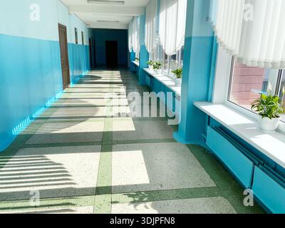 Well-lit corridor with blue and green walls, large windows with blinds, and potted plants on windowsills, providing a calm and inviting indoor space Stock Photo