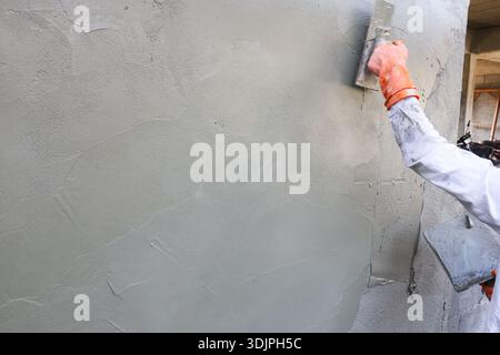 Professional construction worker focused on applying smooth gray plaster to wall with trowel demonstrating skilled craftsmanship and dedicated effort Stock Photo