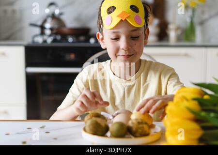 Smiling child wearing bunny ears with natural Easter eggs at home kitchen Stock Photo