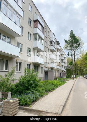 Khrushchev-era apartment building featuring multiple balconies and surrounding greenery, located along a paved sidewalk in an urban environment Stock Photo