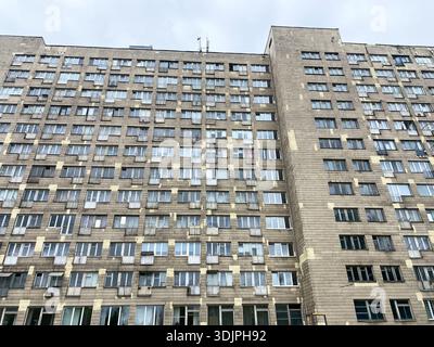 Unappealing dormitory structure featuring many windows and air conditioning units, set against a cloudy sky in an urban environment Stock Photo