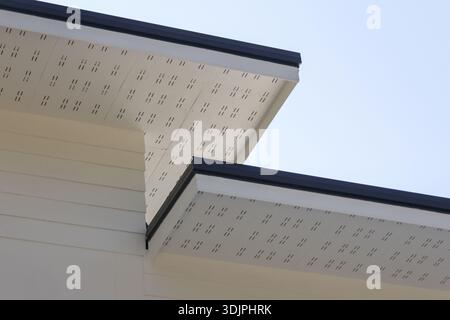 Low angle view of modern eaves with perforated ventilation pattern under beige cream roof showing minimalist architectural detail against clear blue s Stock Photo