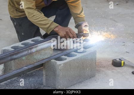 Serious male welder working hard with tool cutting iron pipe with bright sparks and flashes in dangerous industrial workshop construction site outdoor Stock Photo