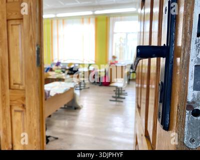View from the entrance of a primary school classroom featuring wooden door, colorful walls, and empty desks ready for students in a bright setting Stock Photo