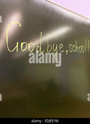 Handwritten text on a dark green chalkboard reads "Goodbye, school" with a classroom setting visible in the background Stock Photo