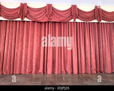 Red velvet curtains with intricate draping and folds serve as an elegant backdrop for a theater stage, enhancing the visual appeal of performances Stock Photo