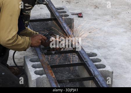 Focused worker using power grinder tool to cut metal frame with bright sparks flying while concentrated on heavy construction job outdoors on concrete Stock Photo