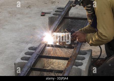 Concentrated male worker cutting steel frame with electric grinder causing bright sparks on construction site showing industrial hard work and focused Stock Photo