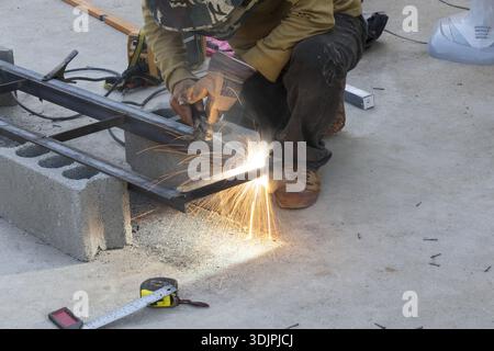 Focused male welder working on metal frame construction project creating bright sparks with professional tool Stock Photo