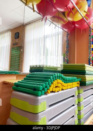 Brightly colored sports equipment is organized in a kindergarten classroom, featuring mats, stacking blocks, and balloons, creating a vibrant learning Stock Photo