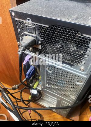Rear view of a computer tower displaying power supply connections, multiple cables, and a ventilation grill, with dust visible on the surface and wood Stock Photo