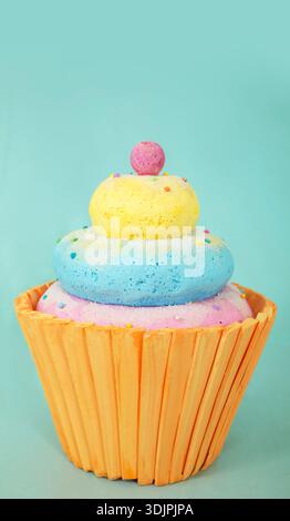Artificial cupcake crafted from polystyrene foam features vibrant blue, yellow, and pink layers with a pink ball on top, set against a light blue back Stock Photo