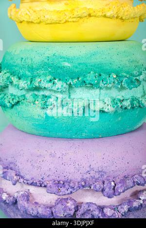 Colorful artificial macarons crafted from polystyrene foam, stacked in yellow, green, and purple, set against a soft blue backdrop Stock Photo