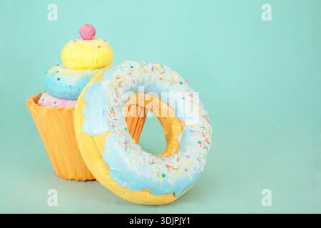 Artificial sweets crafted from polystyrene foam include a cupcake and a donut with blue icing and colorful sprinkles, displayed on a light blue backgr Stock Photo