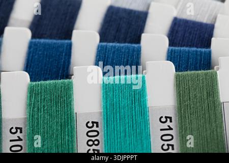 A close-up, angled shot features a collection of cool-toned green and blue thread swatches wrapped around white cardboard tabs, each marked with a dis Stock Photo