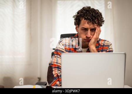 Despaired and exhausted young businessman having a headache while working on laptop at his home. Stock Photo