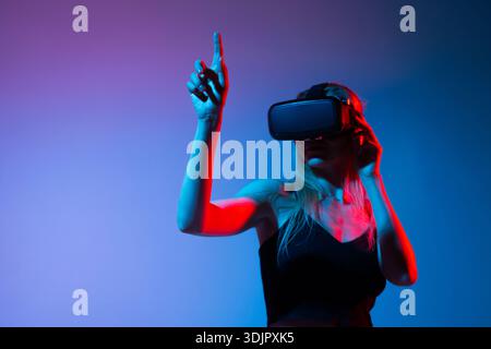 Woman using VR headset and pointing upward in virtual space, immersive gesture interaction and futuristic technology concept Stock Photo