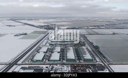 Aerial view of a vast, snow-dusted landscape punctuated by the geometric shapes of data centers, their green roofs contrasting with the white fields, Stock Photo