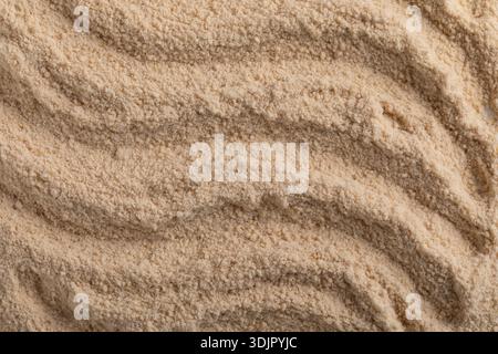 A top-down macro photo shows a uniform layer of high-quality beige herbal powder, with a series of horizontal ridges and a smooth, matte texture. Stock Photo