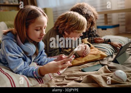 Generation Alpha Children Using Gadgets While Relaxing Indoors Together Stock Photo