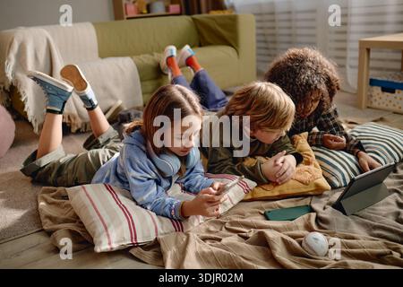 Generation Alpha Children Using Gadgets While Lying on Floor Indoors Together Stock Photo