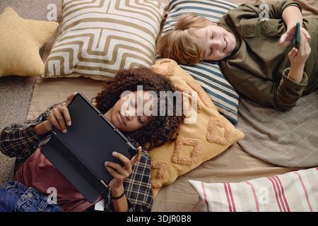 Multiethnic Generation Alpha Children Using Gadgets While Relaxing Indoors Stock Photo