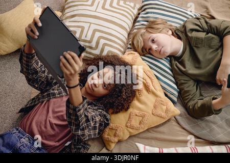 Multiethnic Generation Alpha Children Lying on Floor Using Digital Tablet Together Stock Photo