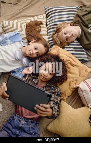 Multiethnic Generation Alpha Children Lying on Pillows Using Digital Tablet Stock Photo
