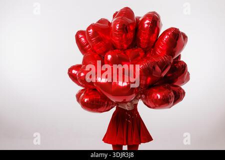 Studio shot of person hidden behind bunch of red heart balloons on white background with copy space for Valentine advertising banner or social media. Stock Photo