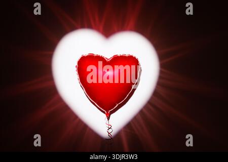 Single red heart foil balloon centered on glowing heart backdrop with copy space, ideal for Valentines Day website banner, ad, or social post. Stock Photo