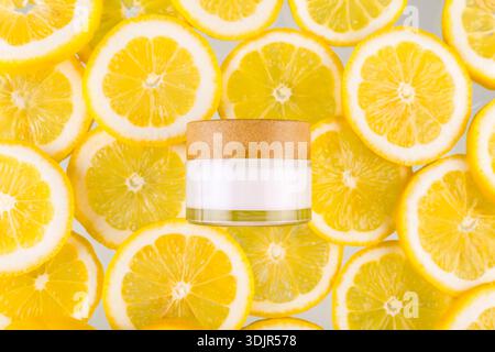 Top view photo of white jar of cream bottle without label in the middle halves and whole yellow lemons on yellow background with blank space Stock Photo