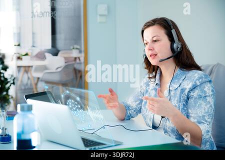 Professional woman interacts with agentic AI hologram and whiteboard. Innovation, future of work, and digital transformation concept. Real people. Stock Photo