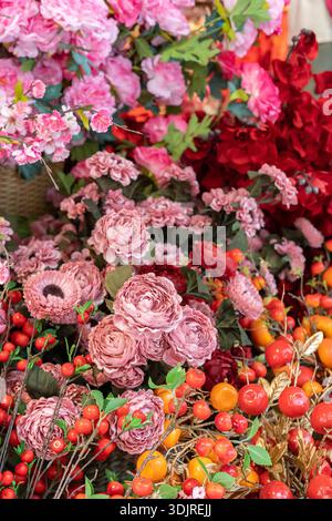 Artificial rich pink roses, carnations, and peonies mingle with bright red berries and lush foliage in a vibrant floral arrangement. Stock Photo
